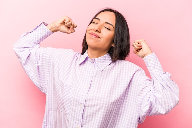 Young hispanic woman isolated on pink background stretching arms relaxed position