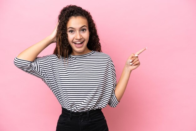 Young hispanic woman isolated on pink background surprised and pointing finger to the side