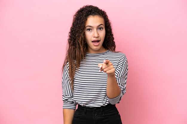 Young hispanic woman isolated on pink background surprised and pointing front