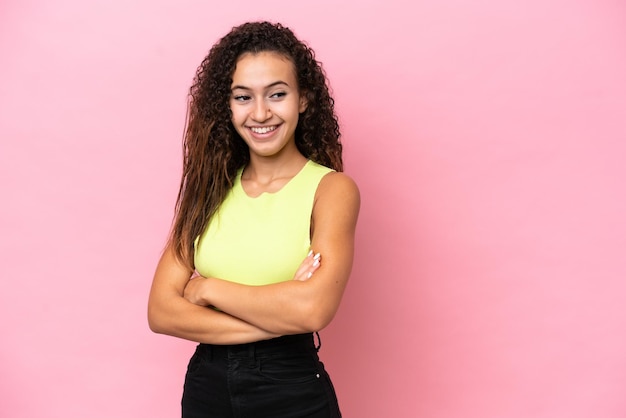 Young hispanic woman isolated on pink background with arms crossed and happy