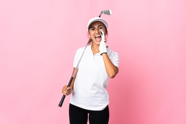 Young hispanic woman over isolated pink playing golf and shouting with mouth wide open