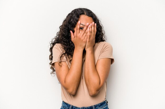 Young hispanic woman isolated on white background blink at the camera through fingers embarrassed covering face