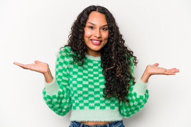 Young hispanic woman isolated on white background makes scale with arms feels happy and confident