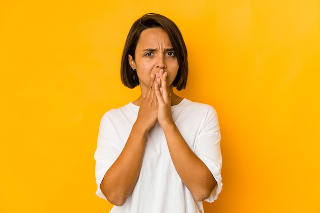 Young hispanic woman isolated on yellow covering mouth with hands looking worried.