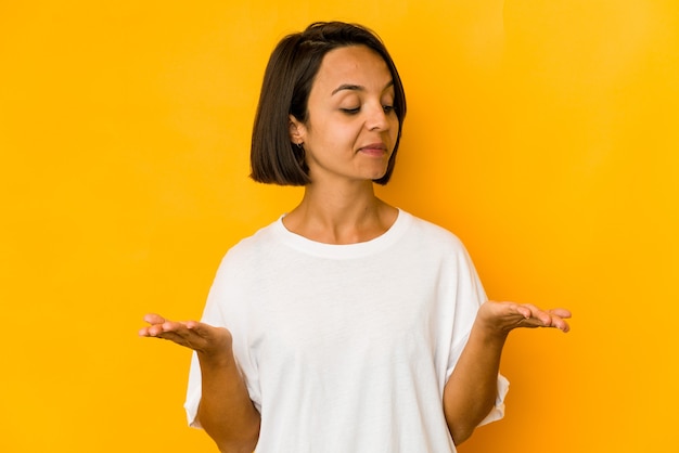 Young hispanic woman isolated on yellow holding something with palms