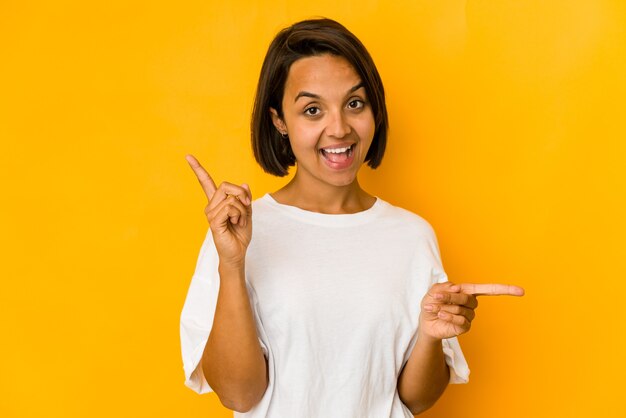 Young hispanic woman isolated on yellow pointing to different copy spaces, choosing one of them, showing with finger.