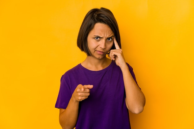 Young hispanic woman isolated on yellow pointing temple with finger, thinking, focused on a task