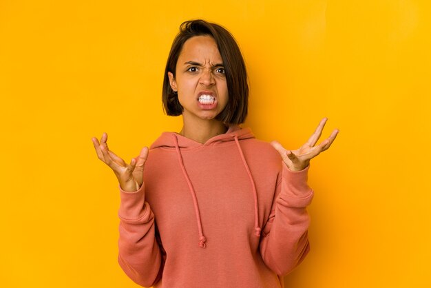 Young hispanic woman isolated on yellow screaming with rage.