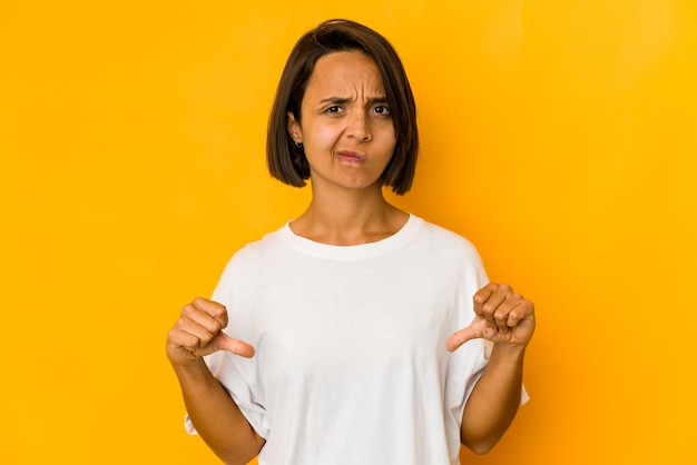 Young hispanic woman isolated on yellow showing a dislike gesture, thumbs down. Disagreement concept.