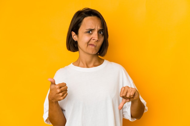 親指を上に、親指を下に、黄色で隔離の若いヒスパニック系女性、難しい選択の概念