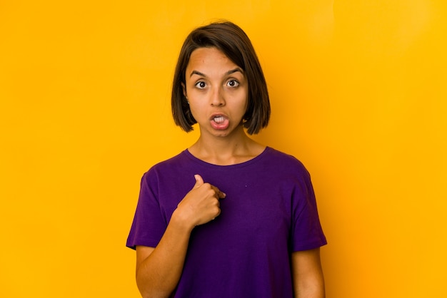 Young hispanic woman isolated on yellow surprised pointing with finger, smiling broadly