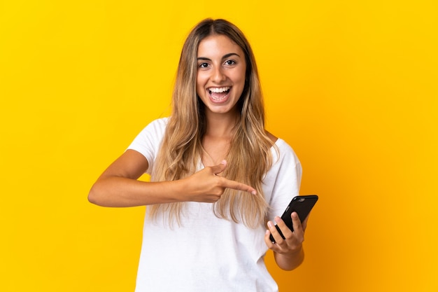 Young hispanic woman over isolated yellow using mobile phone and pointing it