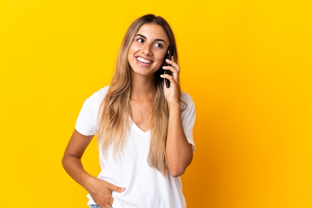 Giovane donna ispanica sopra la parete gialla isolata che mantiene una conversazione con il telefono cellulare con qualcuno