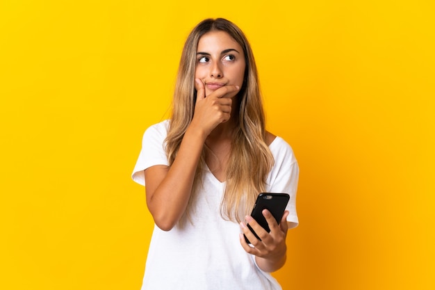 Young hispanic woman over isolated yellow wall using mobile phone and thinking