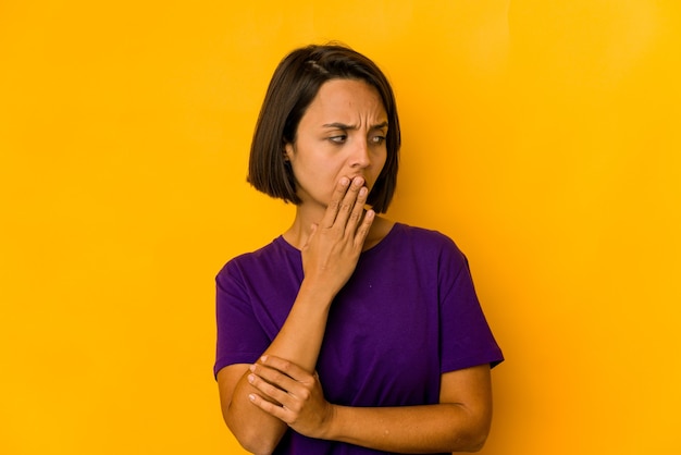 手で口を覆う疲れたジェスチャーを示す黄色のあくびで孤立した若いヒスパニック系の女性。
