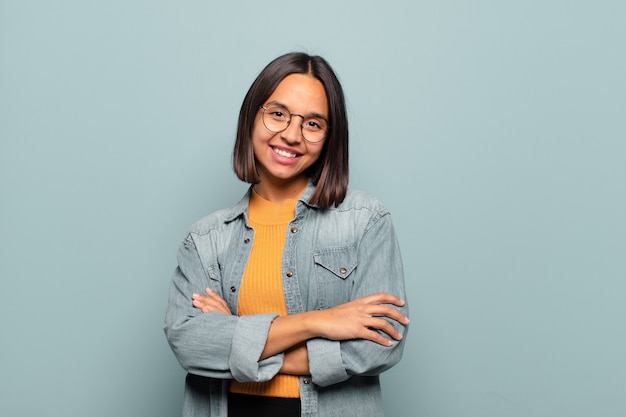 young hispanic woman laughing happily with arms crossed, with a relaxed, positive and satisfied pose