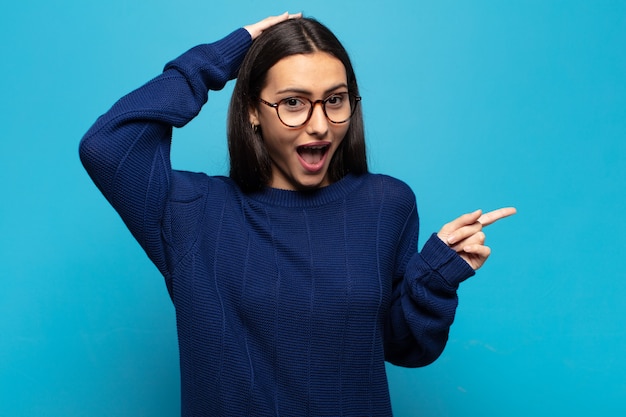 Young hispanic woman laughing, looking happy, positive and surprised, realizing a great idea pointing to lateral copy space