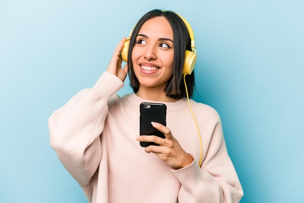 Young hispanic woman listening to music isolated on blue background