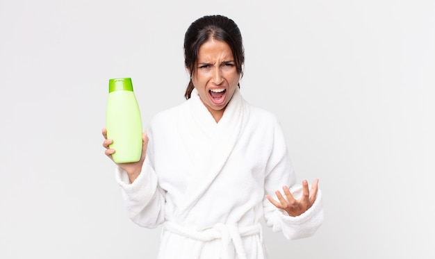 Young hispanic woman looking angry, annoyed and frustrated wearing bathrobe and holding a shampoo
