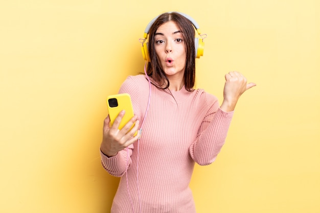 Young hispanic woman looking astonished in disbelief. headphones and telephone concept