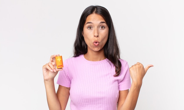 Young hispanic woman looking astonished in disbelief and holding batteries