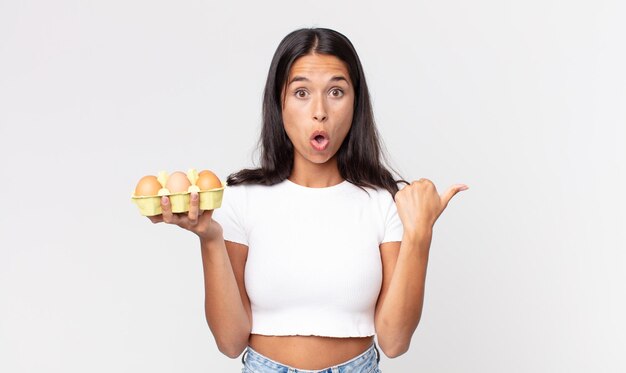 Young hispanic woman looking astonished in disbelief and holding an eggs box