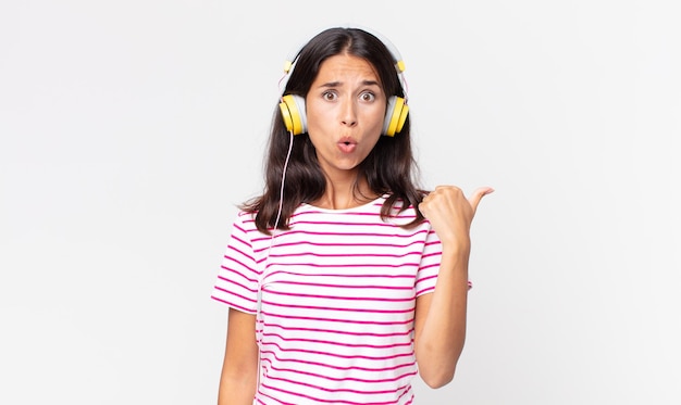 Young hispanic woman looking astonished in disbelief listening music with headphones