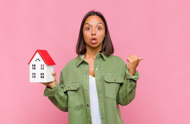 Young hispanic woman looking astonished in disbelief, pointing at object on the side and saying wow, unbelievable