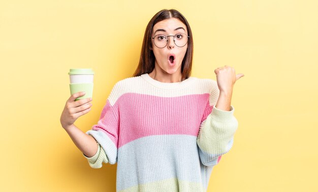 Young hispanic woman looking astonished in disbelief. take away coffee concept