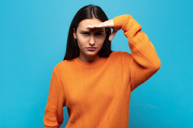 Foto giovane donna ispanica che sembra sconcertata e stupita, con la mano sulla fronte che guarda lontano, guardando o cercando