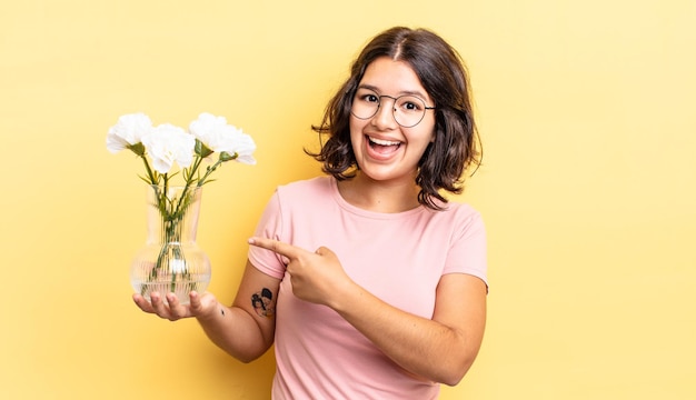 Young hispanic woman looking excited and surprised pointing to the side flowers pot concept