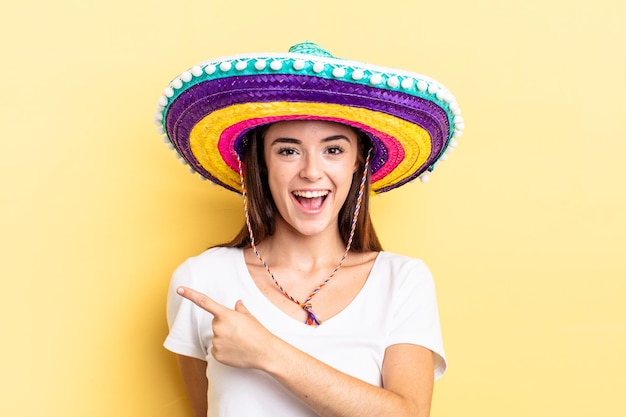 Young hispanic woman looking excited and surprised pointing to the side. mexican hat concept