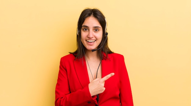 Young hispanic woman looking excited and surprised pointing to the side telemarketer concept