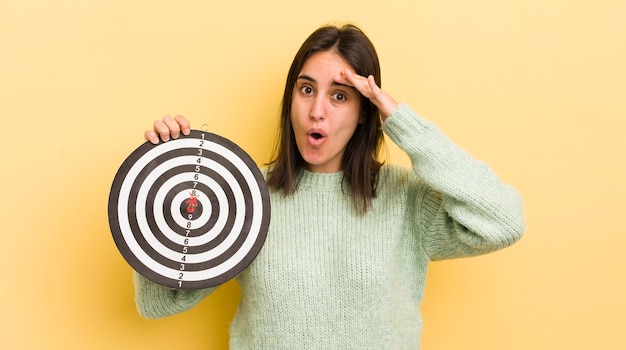Photo young hispanic woman looking happy astonished and surprised darts target concept
