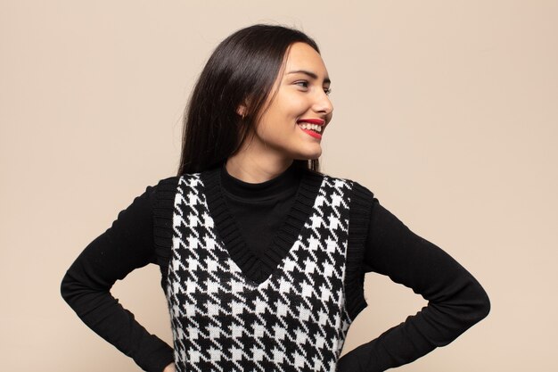 young hispanic woman looking happy, cheerful and confident, smiling proudly and looking to side with both hands on hips