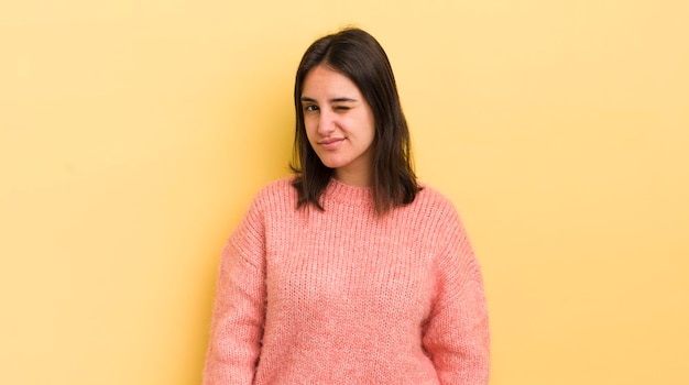 Young hispanic woman looking happy and friendly smiling and winking an eye at you with a positive attitude