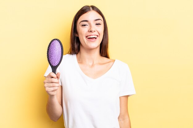 Young hispanic woman looking happy and pleasantly surprised. hair brush concept