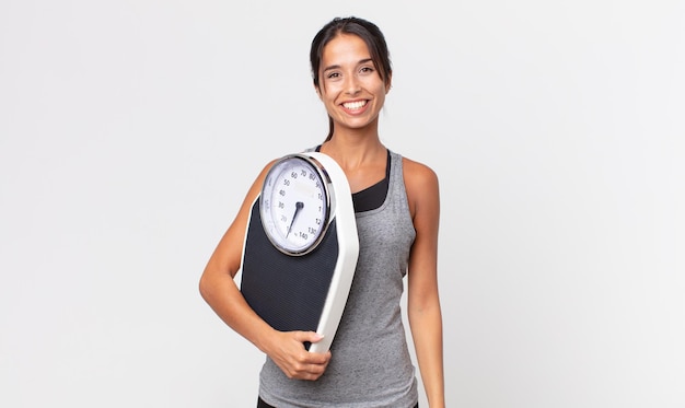 Young hispanic woman looking happy and pleasantly surprised and holding a weight scale. diet concept