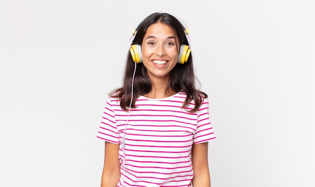 Молодая латиноамериканская женщина выглядит счастливой и приятно удивленной, слушая музыку в наушниках