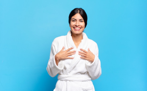 Young hispanic woman looking happy, surprised, proud and excited, pointing to self. bathrobe concept