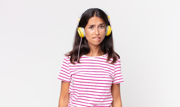 Young hispanic woman looking puzzled and confused listening music with headphones