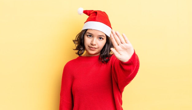 Giovane donna ispanica che sembra seria mostrando palmo aperto che fa gesto di arresto. concetto di natale