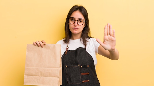 Foto giovane donna ispanica che sembra seria mostrando il palmo aperto facendo gesto di arresto fast food consegnare il concetto