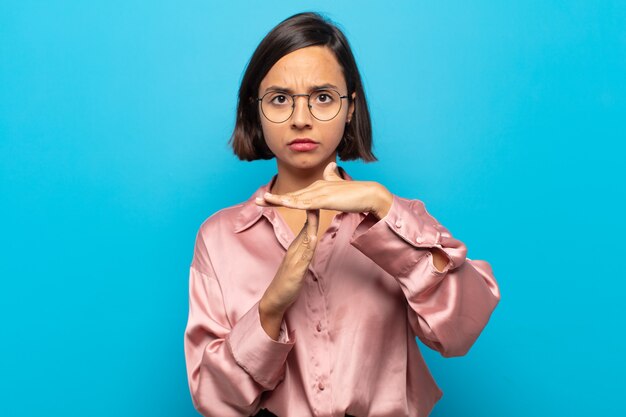 Young hispanic woman looking serious, stern, angry and displeased, making time out sign