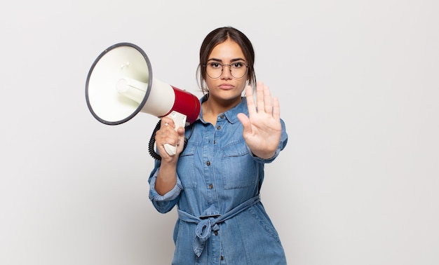 Young hispanic woman looking serious, stern, displeased and angry showing open palm making stop gesture