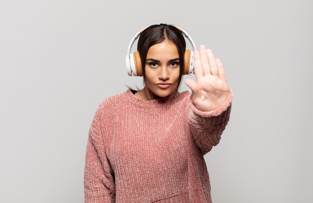 Young hispanic woman looking serious, stern, displeased and angry showing open palm making stop gesture