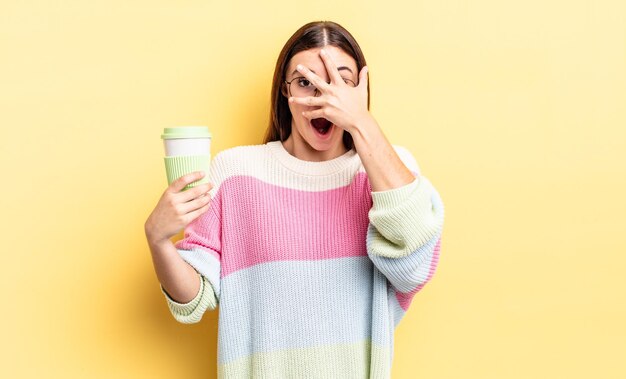 Young hispanic woman looking shocked, scared or terrified, covering face with hand. take away coffee concept