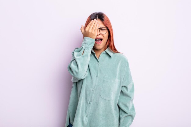 Young hispanic woman looking sleepy, bored and yawning, with a headache and one hand covering half the face