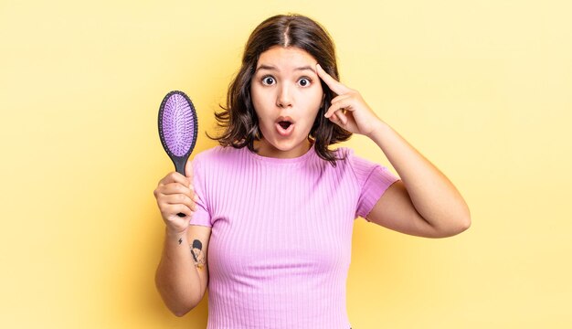 Young hispanic woman looking surprised, realizing a new thought, idea or concept. hairbrush concept