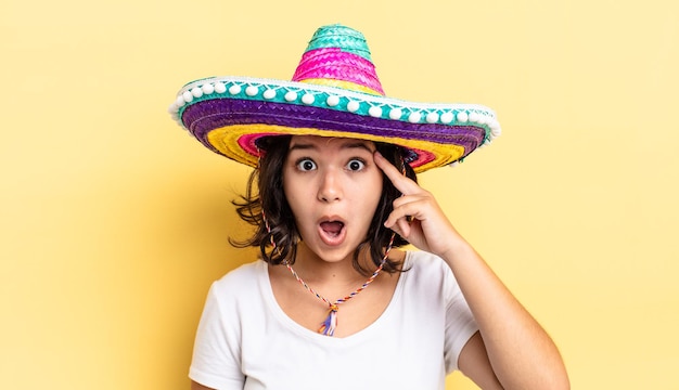 Молодая латиноамериканская женщина выглядит удивленной, осознавая новую мысль, идею или концепцию. концепция мексиканской шляпы